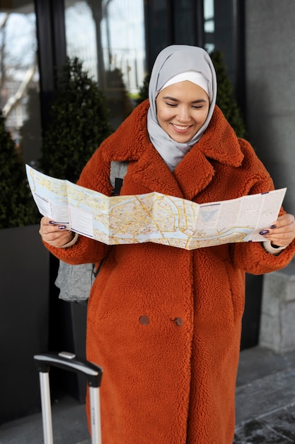 Mujer musulmana consultando un mapa y sonriendo mientras está de vacaciones