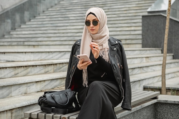 Mujer musulmana con hijab negro y ropa oscura caminando por el edificio  gris de la ciudad. la dama con expresión divertida representa el espacio de  copia de la cultura islámica.