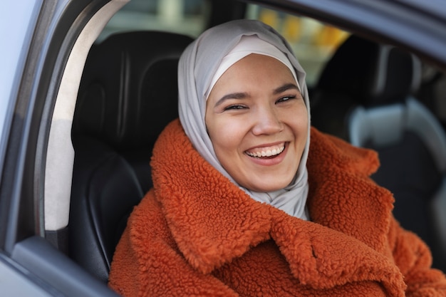 Mujer musulmana con hiyab sonriendo y explorando la ciudad con un auto mientras está de vacaciones