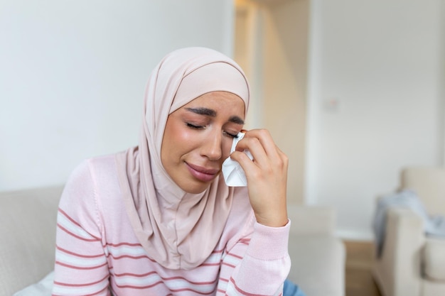 Mujer musulmana joven sentada en la habitación sintiendo dolor con el problema de la vida Mujer musulmana llorando sosteniendo la mano dolorosa que sufre de violencia del marido