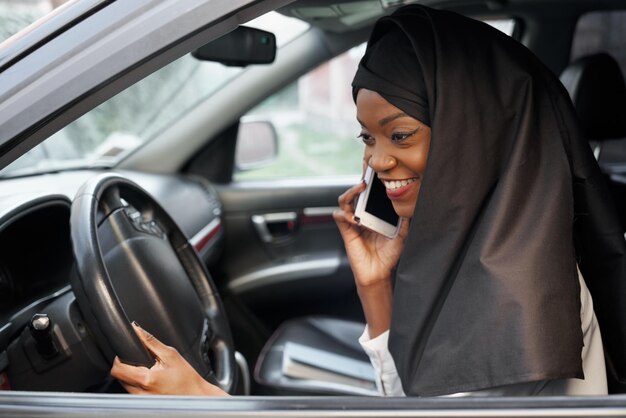 Mujer musulmana sentada en un auto hablando por teléfono móvil