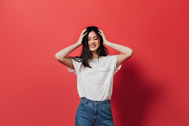 Mujer de muy buen humor despeina su cabello y sonríe contra la pared roja