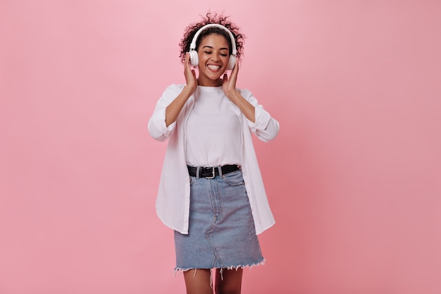 Mujer de muy buen humor está escuchando música con auriculares en la pared rosa