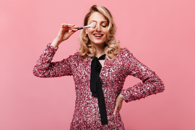Foto gratuita mujer de muy buen humor posando con pincel de maquillaje en pared rosa