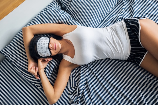 Mujer muy sexy acostada en la cama por la mañana, se despierta temprano, durmiendo con máscara