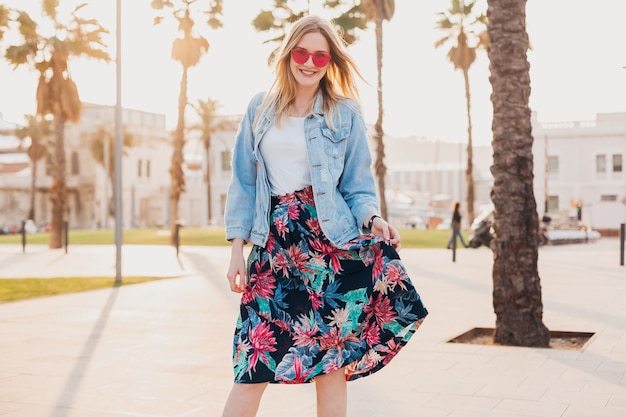 Foto gratuita mujer muy sonriente caminando en las calles de la ciudad con elegante falda estampada y chaqueta vaquera de gran tamaño con gafas de sol rosas, tendencia de estilo veraniego