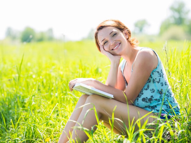 Mujer muy sonriente lee el libro en la naturaleza