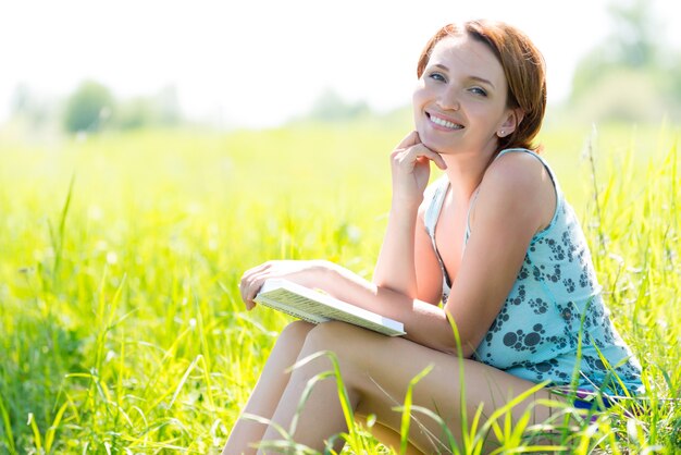 Mujer muy sonriente lee el libro en la naturaleza