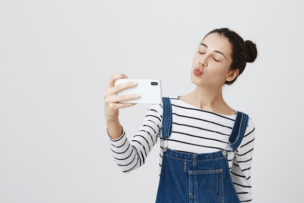 Mujer muy sonriente tomando selfie en smartphone, haciendo pucheros por beso