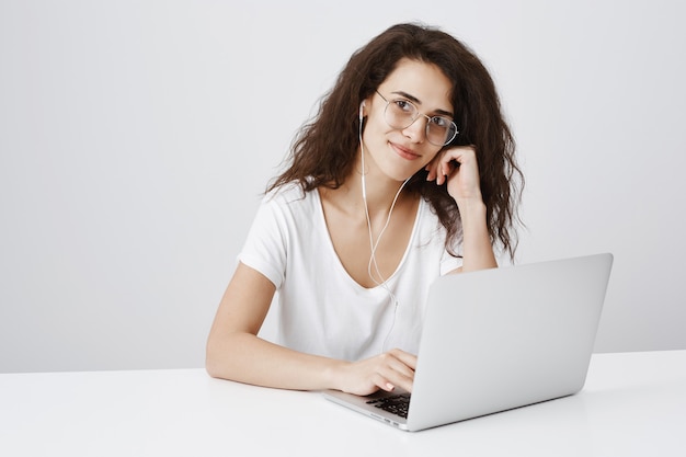 Mujer muy sonriente trabajando en un proyecto a través de una computadora portátil y un escritorio sentado