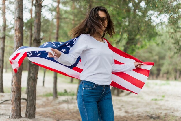 Mujer en naturaleza sujetando bandera americana
