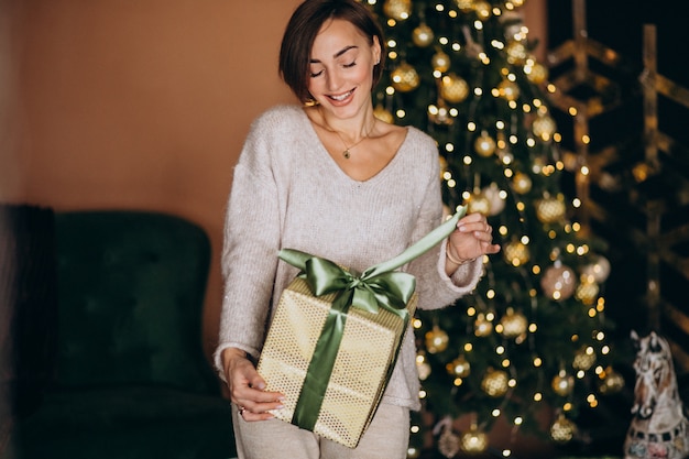 Mujer en navidad sosteniendo un regalo de navidad junto al árbol de navidad