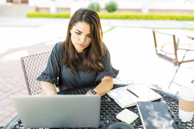 Mujer de negocios adulta media concentrada usando una computadora portátil en la mesa en el jardín