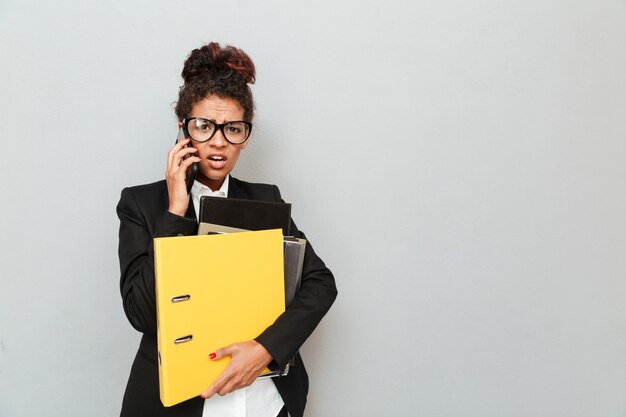 Mujer de negocios africana joven confusa que sostiene carpetas.