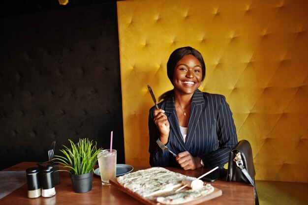 Mujer de negocios afroamericana comiendo pizza de queso en la cafetería Chica negra descansando