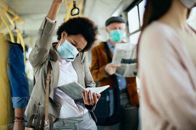 Mujer de negocios afroamericana con mascarilla protectora mientras viaja en autobús