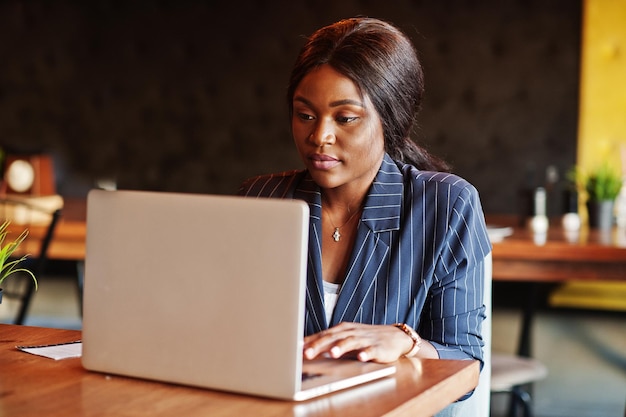 Mujer de negocios afroamericana sentada en la mesa en el café Chica negra trabajando con una computadora portátil