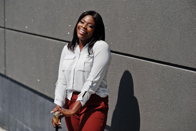 Mujer de negocios afroamericana vestida formalmente con blusa blanca y pantalón rojo con bastón en la mano Exitosa mujer de negocios de piel oscura