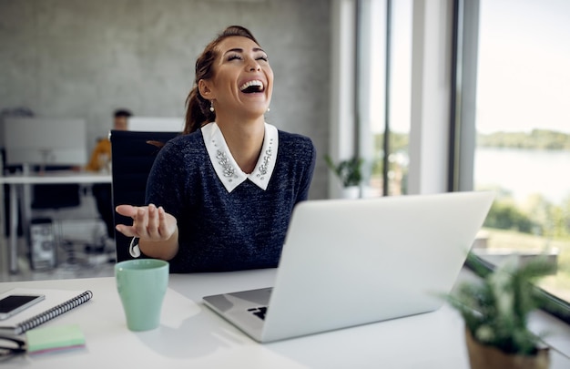 Foto gratuita una mujer de negocios alegre divirtiéndose mientras usa una laptop en la oficina