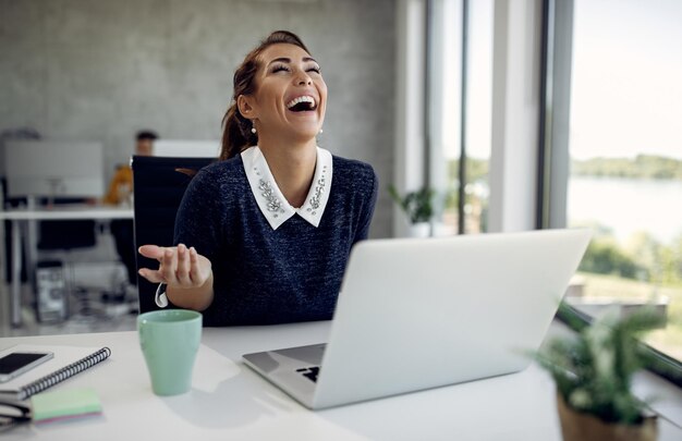 Una mujer de negocios alegre divirtiéndose mientras usa una laptop en la oficina