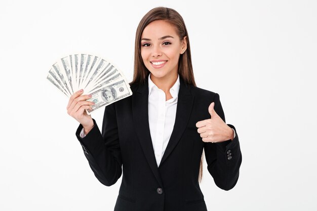 Mujer de negocios alegre mostrando pulgares arriba sosteniendo dinero