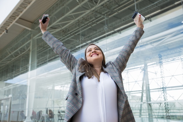 Mujer de negocios alegre que levanta los brazos al aire libre