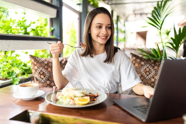 Mujer de negocios almorzando y trabajando en equipo portátil