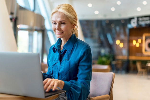 Mujer de negocios anciana sonriente trabajando en equipo portátil mientras está fuera