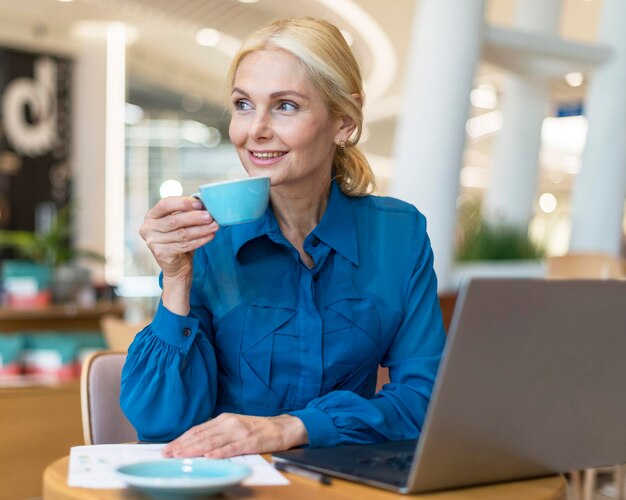 Mujer de negocios anciano sonriente disfrutando de una taza de café mientras trabaja