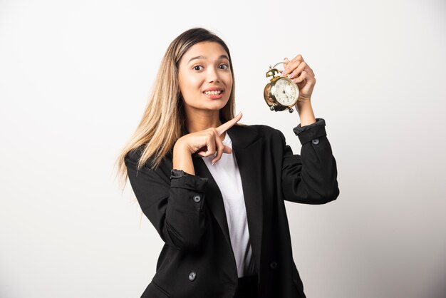 Mujer de negocios apuntando a un reloj de alarma en la pared blanca.