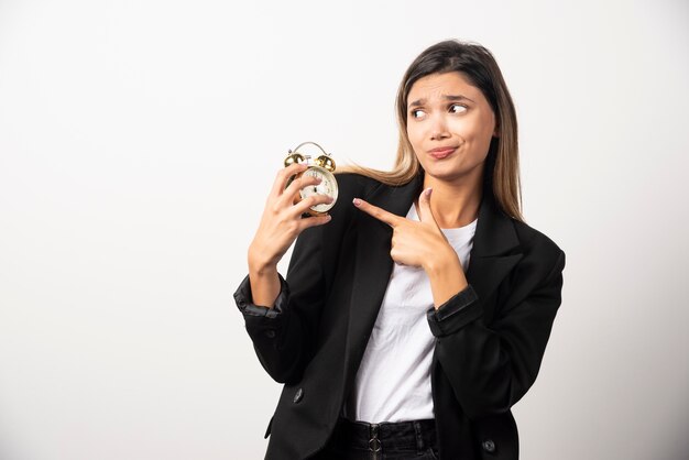 Mujer de negocios apuntando a un reloj de alarma en la pared blanca.