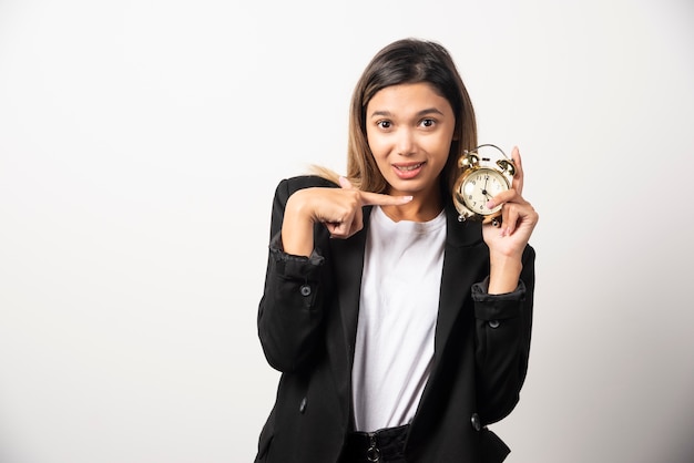 Mujer de negocios apuntando a un reloj de alarma en la pared blanca.