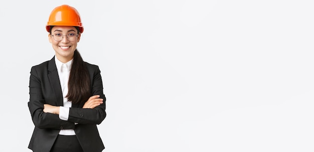 Mujer de negocios asiática sonriente profesional con casco de seguridad y traje de brazos cruzados y con confianza vendiendo nuevos edificios Ingeniero gerente de construcción mostrando saludos a los inversores