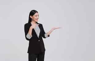 Foto gratuita mujer de negocios asiática en traje de pie con la mano que presenta o muestra señalando el dedo para copiar el espacio