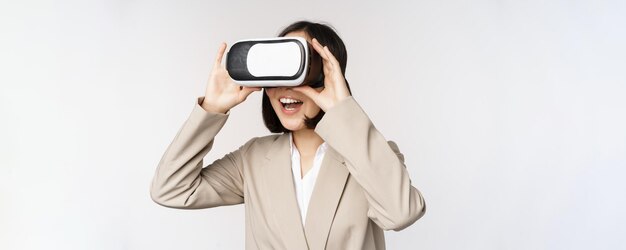 Mujer de negocios asombrada en traje usando gafas de realidad virtual que se ve asombrada en auriculares vr de pie sobre fondo blanco