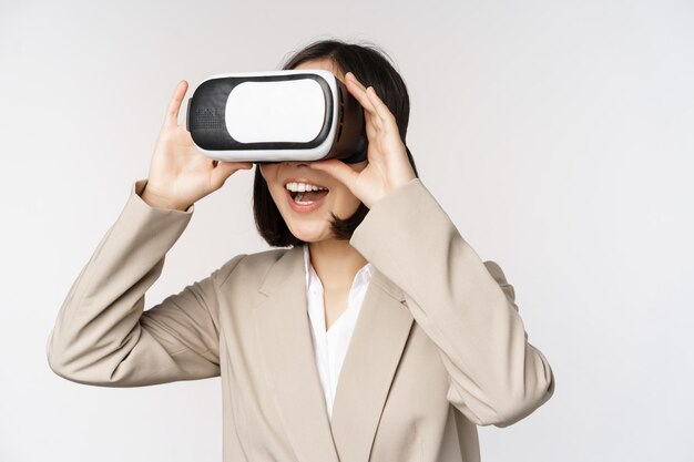 Mujer de negocios asombrada en traje usando gafas de realidad virtual que se ve asombrada en auriculares vr de pie sobre fondo blanco