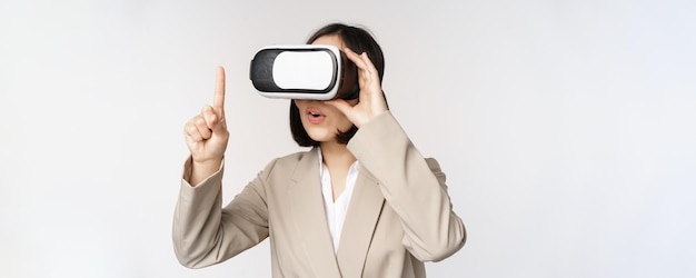 Mujer de negocios asombrada en traje usando gafas de realidad virtual que se ve asombrada en auriculares vr de pie sobre fondo blanco