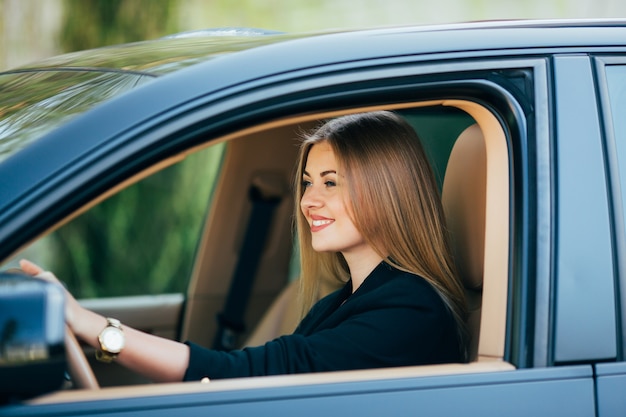 Mujer de negocios atractiva con gafas de sol sonriendo y conduciendo su coche.