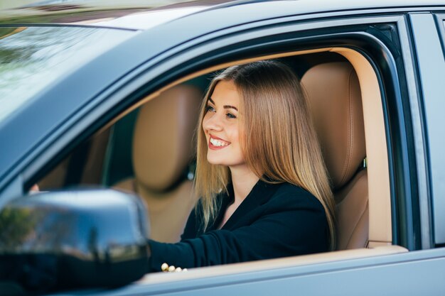 Mujer de negocios atractiva con gafas de sol sonriendo y conduciendo su coche.