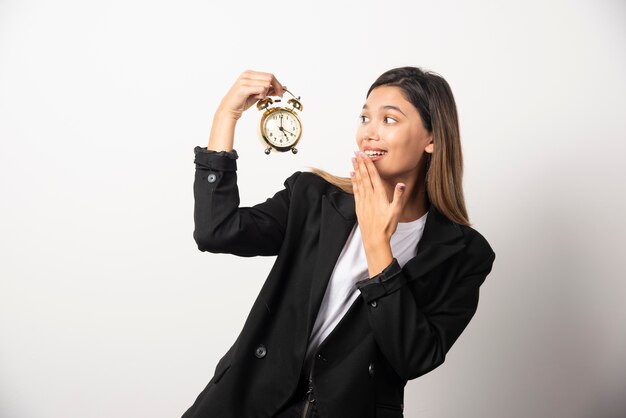 Mujer de negocios en busca de un reloj de alarma en la pared blanca.