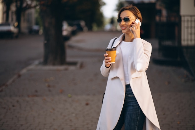 Mujer de negocios con café de consumición del teléfono afuera en calle