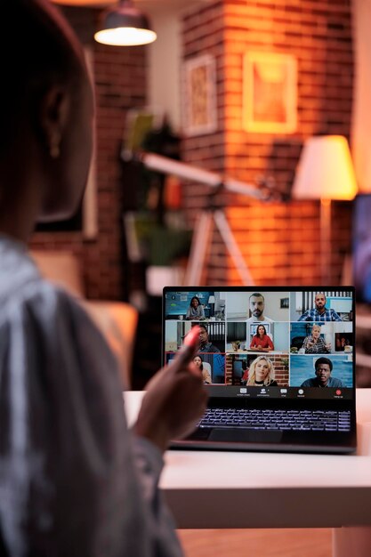 Mujer de negocios charlando con un equipo remoto en teleconferencia usando una laptop, vista posterior. Compañeros de la empresa discutiendo negocios en videollamadas, trabajo en equipo de empleados de oficina y cooperación