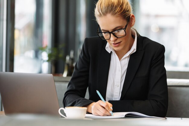 Mujer de negocios concentrada escribiendo notas en el cuaderno.