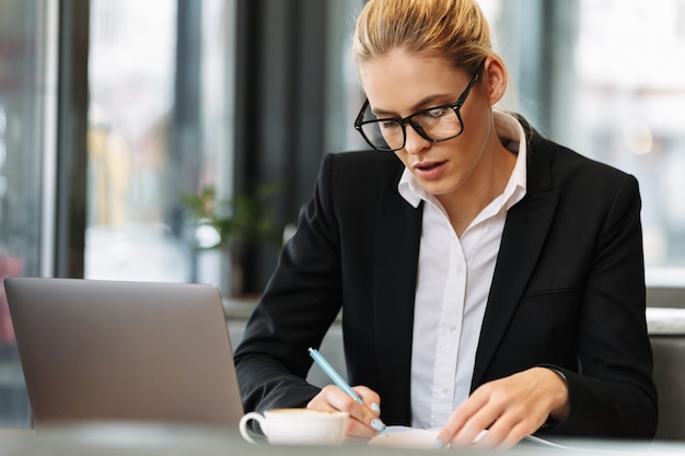 Mujer de negocios concentrada escribiendo notas en el cuaderno.