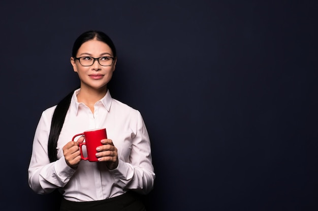 Mujer de negocios disfrutando de un descanso para tomar café sosteniendo una taza roja aislada en un fondo oscuro