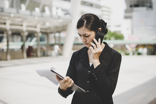 Mujer de negocios con documento en mano hablando por teléfono celular cerca de centro de negocios