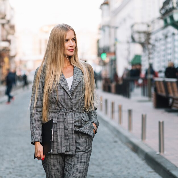 Mujer de negocios elegante andando en ciudad con portapapeles