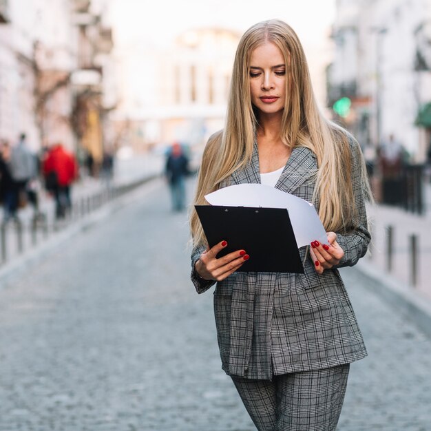 Mujer de negocios elegante andando en ciudad con portapapeles