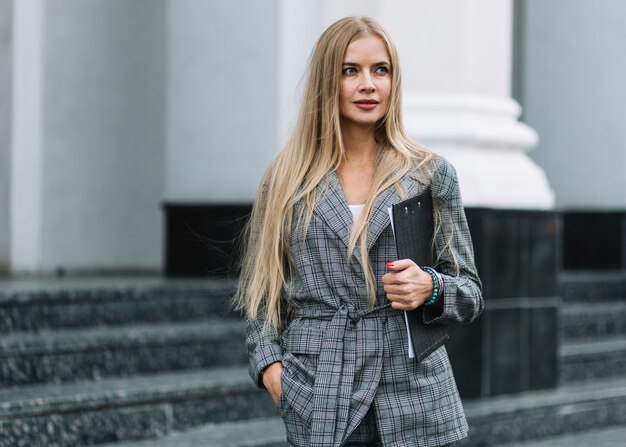 Mujer de negocios elegante andando en ciudad con portapapeles