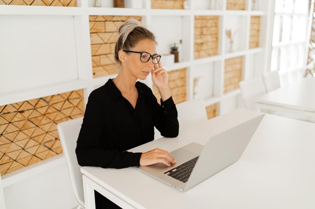 Mujer de negocios con elegante atuendo informal sentada en la oficina y usando una computadora portátil
